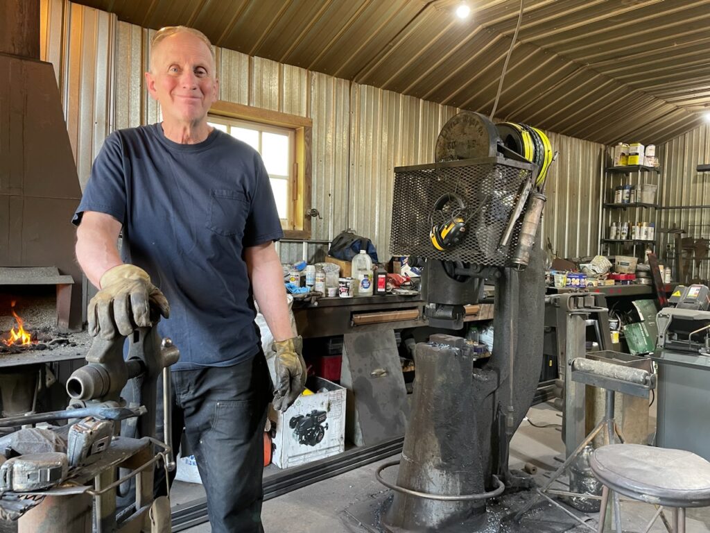 image of Dale Burton standing in his blacksmith shop in front of a coal forge fire